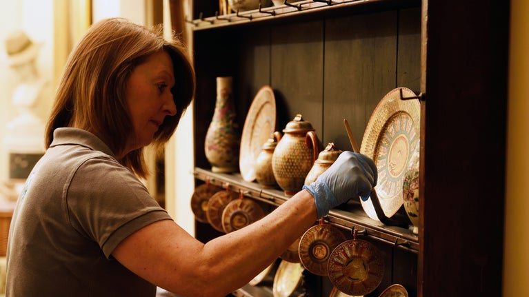 A conservation assistant carefully dusts objects at Greenway, Devon